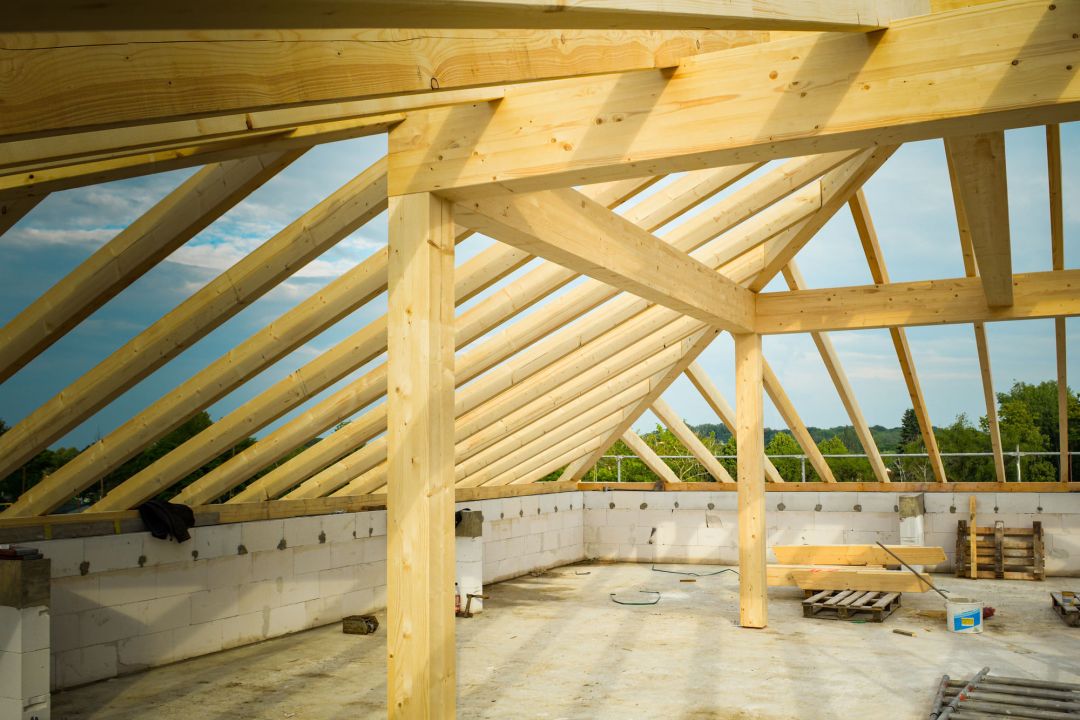 Neu errichtetes Dachtragwerk aus Nadelholz mit Sparren, Mittelpfette und tragender Stütze über einer Massivwand
